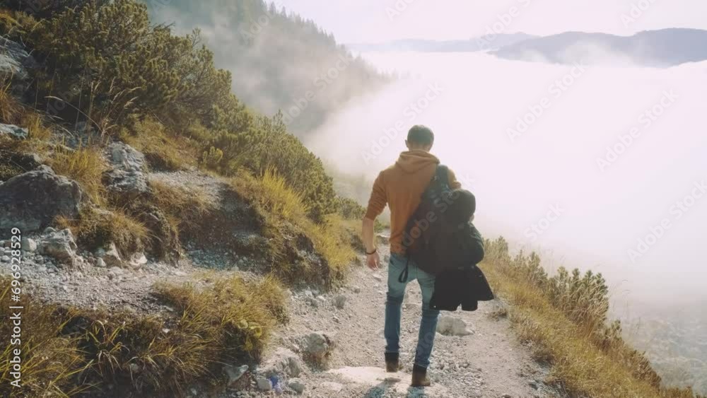 Man traveler walks through the forest higher than clouds to the mountains. Incredibly beautiful views in the Alpine mountains. Hiking route in the Alps mountains in autumn