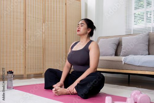 Fat Asian woman stretching at home on a fitness mat. Practicing activities at home online exercise classes Practice stretching on your yoga mat at home to stay healthy and in shape.