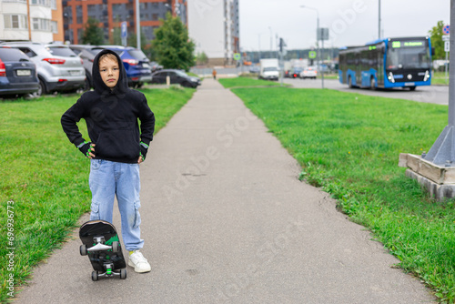 Copy space. Child boy with a skateboard on a city street. A child learns to ride a skateboard on the sidewalk. A stylish boy goes for a walk on a skateboard around the city. Lifestyle.