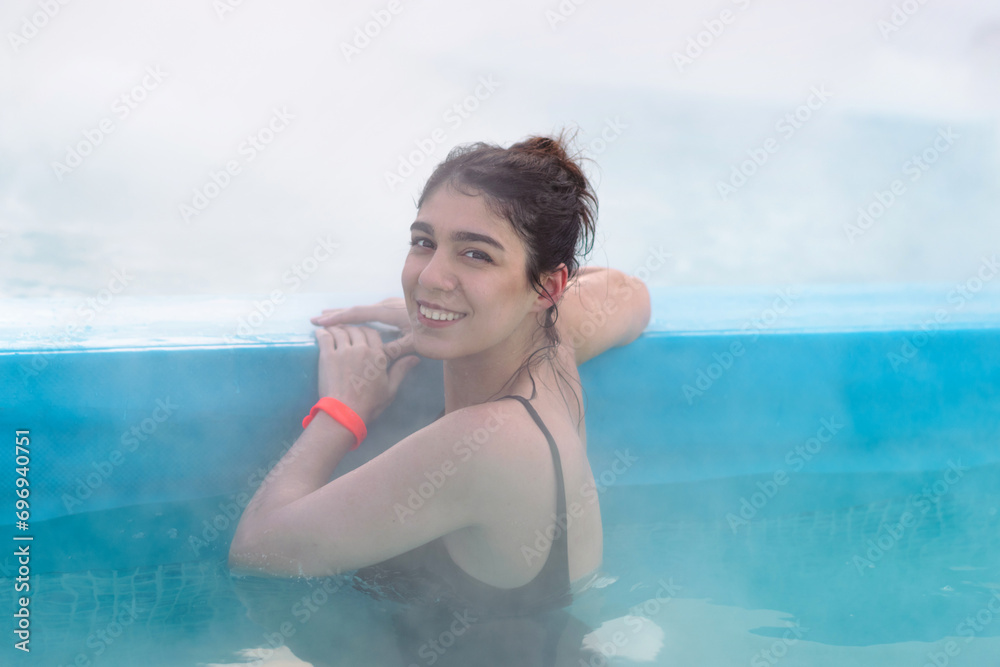 A smiling young dark-haired woman bathes in a hot thermal spring on a winter day.Self-care,healthy lifestyle,leisure activity,mental health concept.
