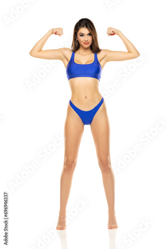 Young beautiful brunette woman in blue bikini swimsuit posing on a white studio background.