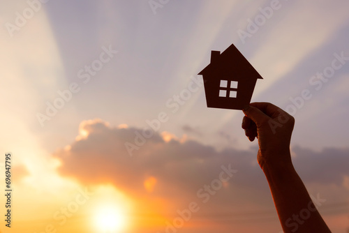 woman hands holding paper house on sunrise, family home, homeless housing, home protection insurance concept, international day of families, new life, foster home care, and real estate. photo