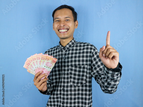 Excited expression handsome asian man hold paper money banknotes with pointing up gesture photo