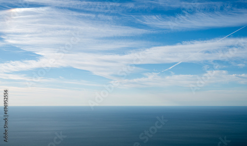 Panoramic beautiful view of a serene horizon where the blue sky with clouds meets the calm sea or ocean.