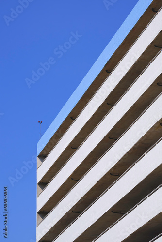 Low angle view of blue and white parking garage building against blue clear sky background in vertical frame © Prapat