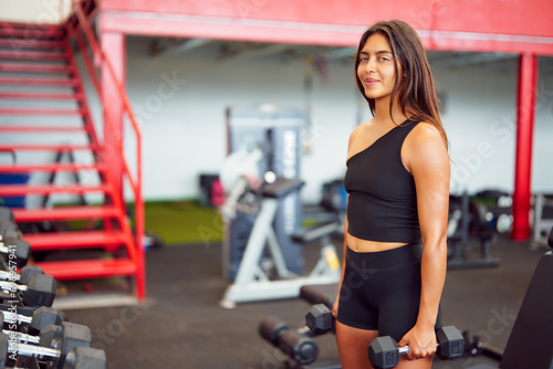 portrait Latin American woman holding dumbells in the gym 