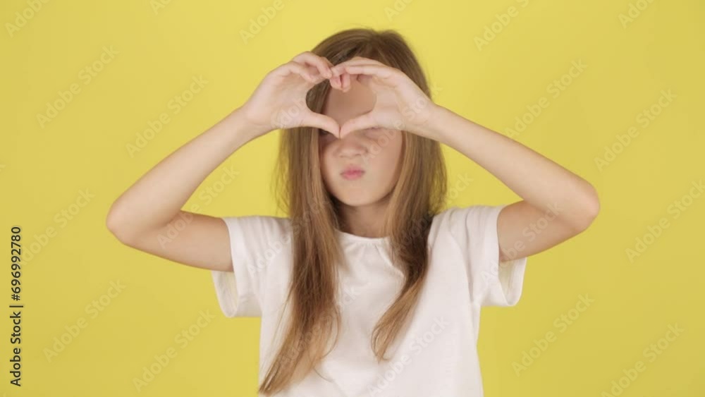 little girl kid demonstrates heart sign with hands, isolated on yellow color background wall in studio. little girl kid demonstrates heart sign with hands, isolated on yellow color background wall in studio.