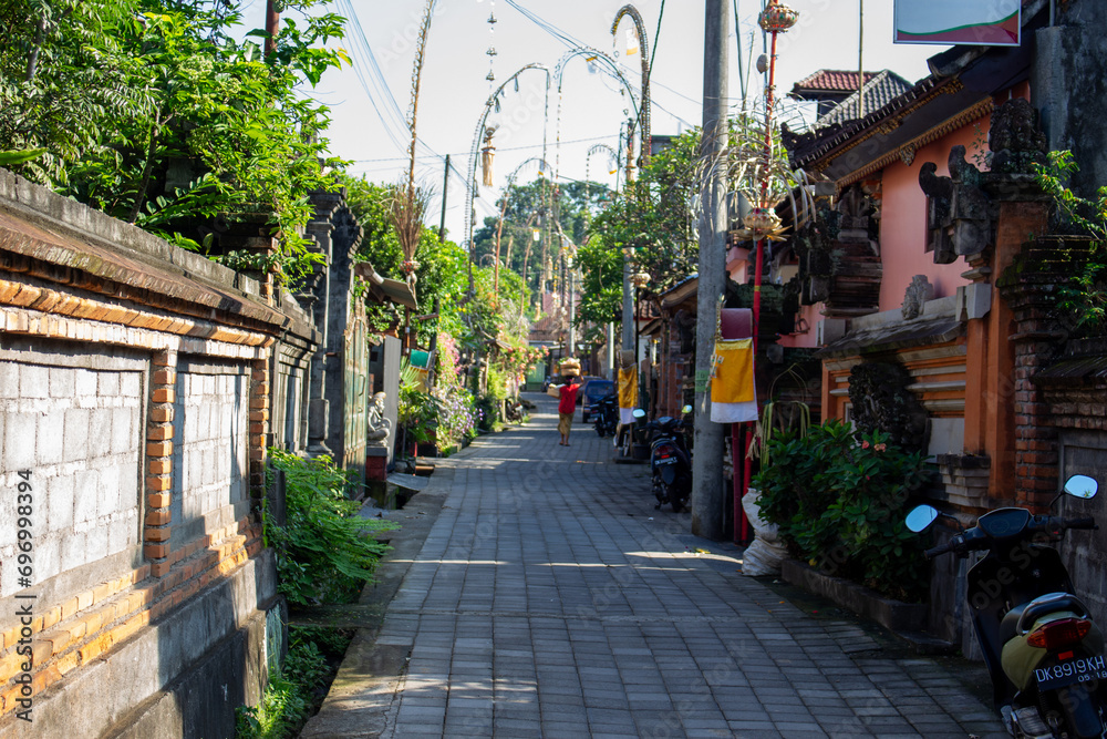 A quiet street in a tropical location flanked by walls and traditional buildings with scooters parked along the side.