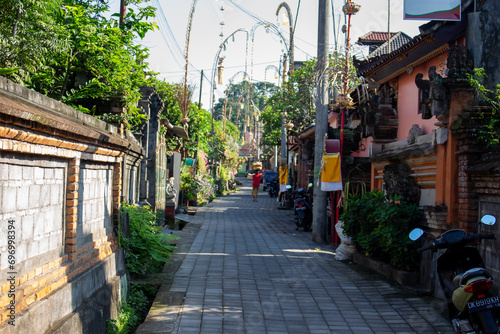 A quiet street in a tropical location flanked by walls and traditional buildings with scooters parked along the side. © Marcel