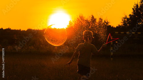 A boy in the setting sun runs across the field with big soap bubbles. Atmospheric photo, vacation, warmth, children's joy, carelessness. High quality photo