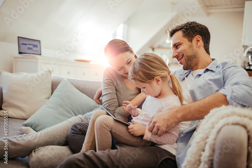 Happy young family sitting on couch with tablet