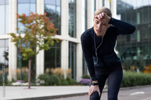 Bilde på lerret Tired athlete runner breathing heavily, resting after long run, senior mature woman active lifestyle, jogging and fitness near park, trees using phone and headphones listening to music , podcasts