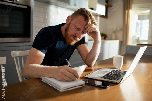 Contemplative man working from home with his laptop and notebook