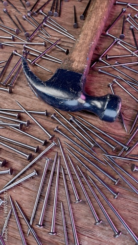 Old stained iron hammer on wooden table surrounded with nails. 3D illustration