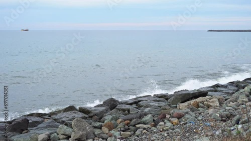 Sea waves hit the rocky shore creating splashes and ship at horison. Calmness and tranquility, meditation and relaxation, a screensaver of natural beauty. Rocky shore and waves photo