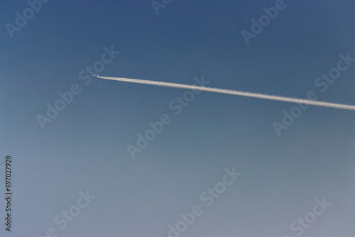 Engine exhaust contrails forming behind the airplane in a blue sky.