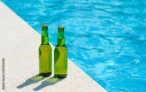 Two bottles of beer stand on the edge of the pool on a summer sunny day. Vacation concept with friends