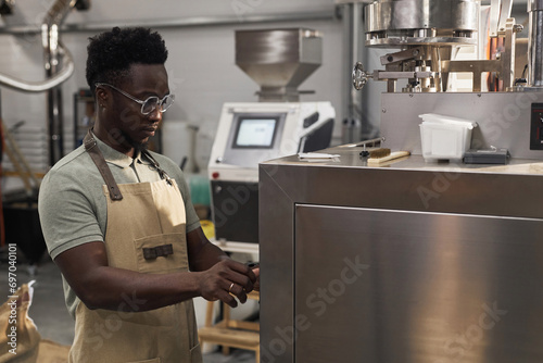 Side view portrait of Black young man operating equipment at coffee production factory, copy space