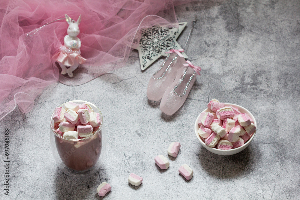 Cocoa with marshmallows, Christmas tree decorations and pink tulle on a concrete background.