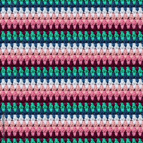Seamless knitted texture in afghan style. The pattern is crocheted from multicolored cotton yarn. Textured blanket.