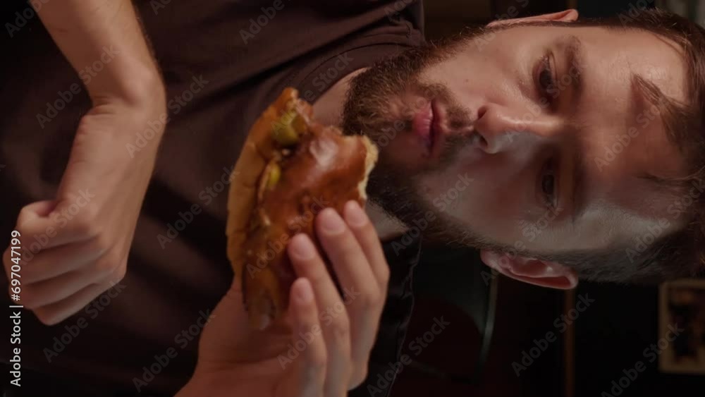 fanny bearded hungry man Biting Burger in Fast Food Restaurant. Portrait of man Eating unhealthy meal and Looking in Camera in Slowmotion. vertical fanny bearded hungry man Biting Burger in Fast Food Restaurant. Portrait of man Eating unhealthy meal and Looking in Camera in Slowmotion. vertical