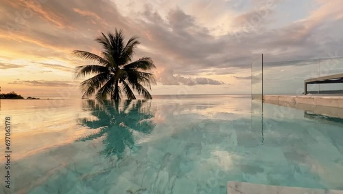 The coast of Thailand on a sunset, The empty swimming pool, coconut palm tree on background, cloudy rainy pink sky above still sea photo