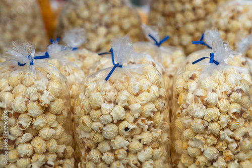 Multiple clear plastic bags of confection containing caramel corn popcorn, for sale by a street vendor. The sweet tasty snack of candy corn is stacked in a green wire basket at a farmer's market stall photo