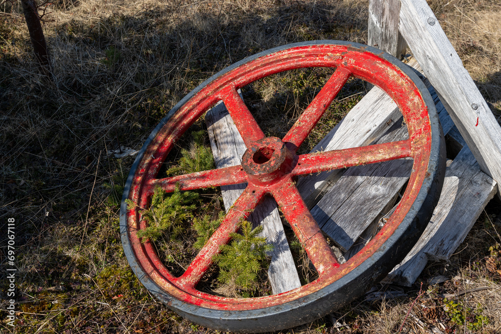 A vintage red wooden spoked, rusty steel rim and center horse-drawn wagon wheel. The antique tire was used on farm equipment, vehicles, stagecoaches and carriages.