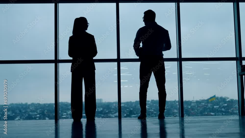 Two full-length silhouettes standing at the window. Male and female stand back to the camera looking at panoramic window. Two full-length silhouettes standing at the window. Male and female stand back to the camera looking at panoramic window.