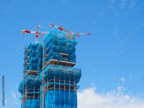 Skyward Ascent: Capturing the Dynamic Symphony of Urban Growth, Steel Giants Rise Amidst Construction Cranes, Against a Canvas of Brilliant Blue Sky