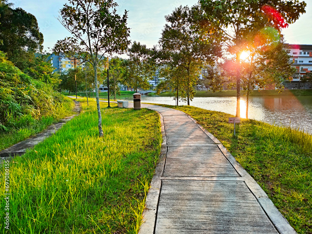 Obraz premium Beautiful park at sunny day UiTM Puncak Alam, Selangor. Small concrete walkway on green grass lawn in park with warm sunset sunlight. Outdoor city park landscape photography.
