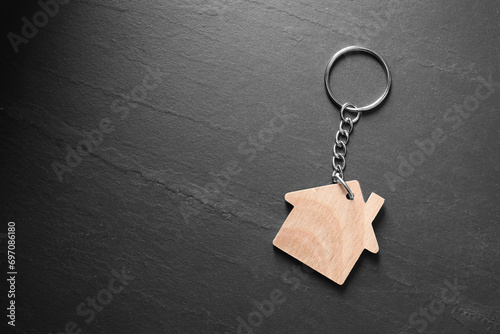 Wooden keychain in shape of house on dark textured table, top view. Space for text photo