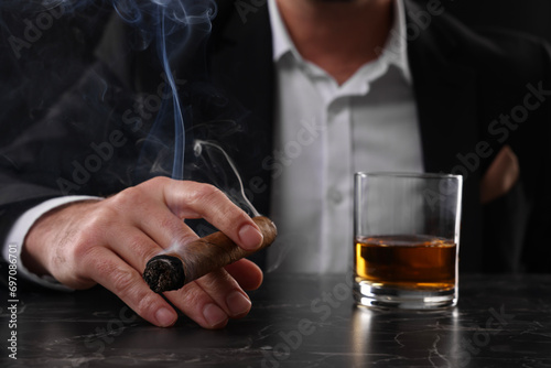 Man with glass of whiskey smoking cigar at dark marble table, closeup