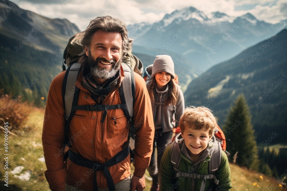 A happy family with backpacks smiles on a mountain hike, with stunning alpine scenery in the background.