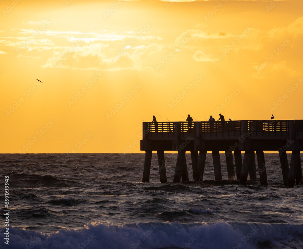 Anglers silhouette against a fiery sunrise at Lake Worth Pier, perfect for themes of leisure and nature. Anglers silhouette against a fiery sunrise at Lake Worth Pier, perfect for themes of leisure and nature.