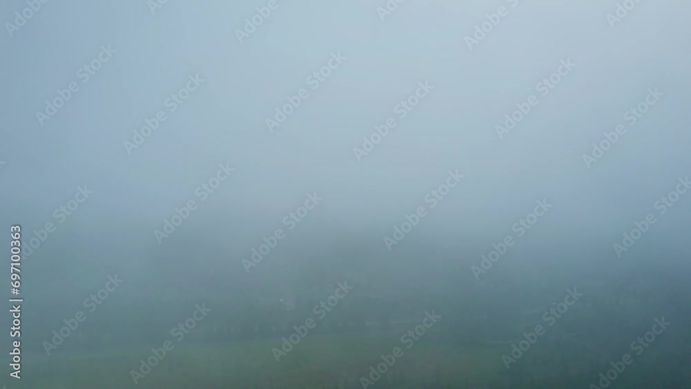 Flying out of the mist revealing the wooden holiday bungalows in Norway. Mountain with houses and pine trees on cloudy summer morning with foggy rainy weather and raindrops on the camera lens of drone Flying out of the mist revealing the wooden holiday bungalows in Norway. Mountain with houses and pine trees on cloudy summer morning with foggy rainy weather and raindrops on the camera lens of drone