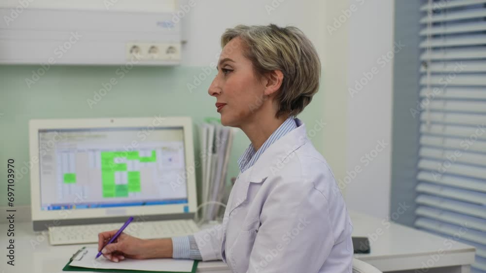 Side view portrait of female doctor making notes on clipboard consulting unrecognizable patient, explaining medical results, giving prescription treatment, appoint consultation sitting in clinic. Side view portrait of female doctor making notes on clipboard consulting unrecognizable patient, explaining medical results, giving prescription treatment, appoint consultation sitting in clinic.