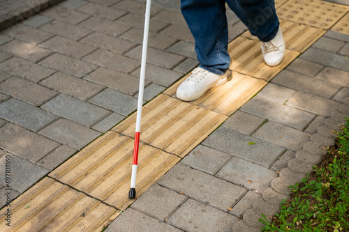 A blind woman walks outdoors using a cane along a tactile yellow tile.