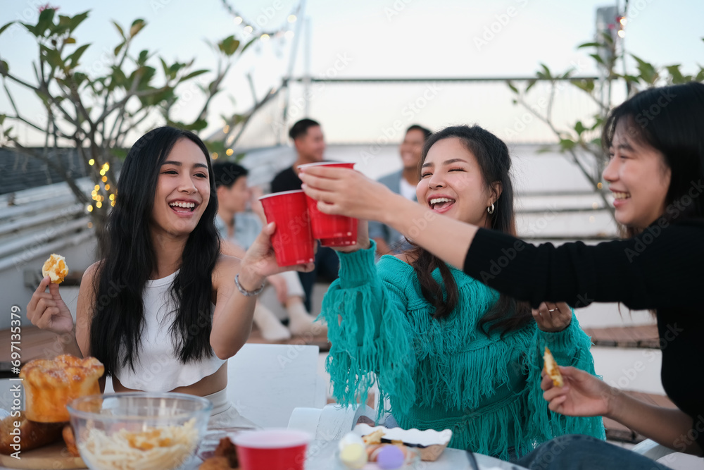 Obraz premium Cheerful male and female friends enjoying happy hour at terrace party and toasting drinks.