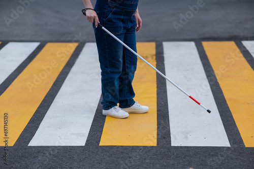 Close-up of the legs of a blind woman crossing the road at a crosswalk with a cane.  photo