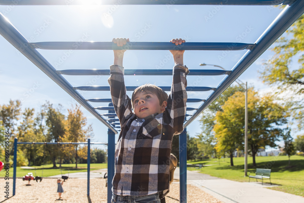Fototapeta premium Young boy does monkey bars at playground with bright sun