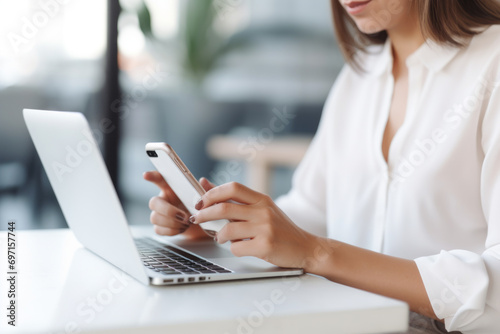 Portrait of a business woman operating a smartphone or laptop keyboard. Chatting and website search on the internet at a white table in a cafe. Online meeting. Global network idea concept.