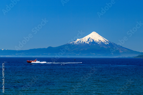 The Osorno Volcano is seen from the banks of Lake Llanquihue, a boat moving in foreground, Puerto Varas, Lake District, Chile photo