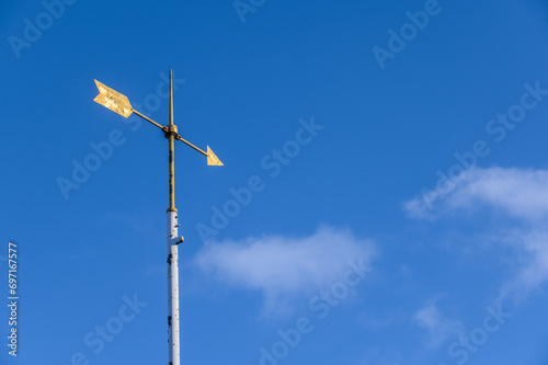 Wetterfahne mit goldenem Pfeil vor blauem Himmel mit Wolken photo