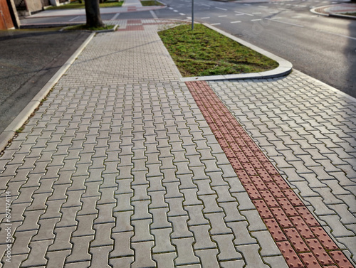 navigation tactile tiles strip for blind and disabled pedestrians who have vision problems. The red pavement has protrusions that lead the person to the crossing and draw attention to the edge road