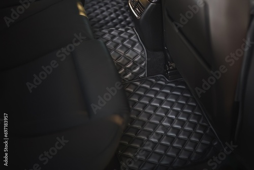 A leather floor mat in the second row of a modern and luxurious car. The interior is black and stylish, with a dashboard that has technology and speed features, a seat, and pedals. photo