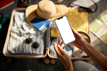 Closeup female hand holding smartphone with empty screen over travel suitcase