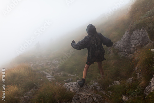 Adult Hiker Descending High Mountain Hiking Trail in Wet Weather Overcast Conditions Rear View