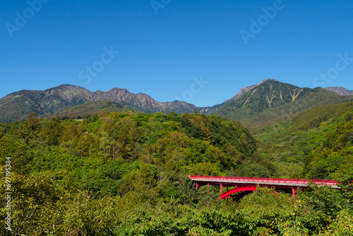 八ヶ岳の麓の森に印象的な赤い東沢大橋、秋晴れの青空