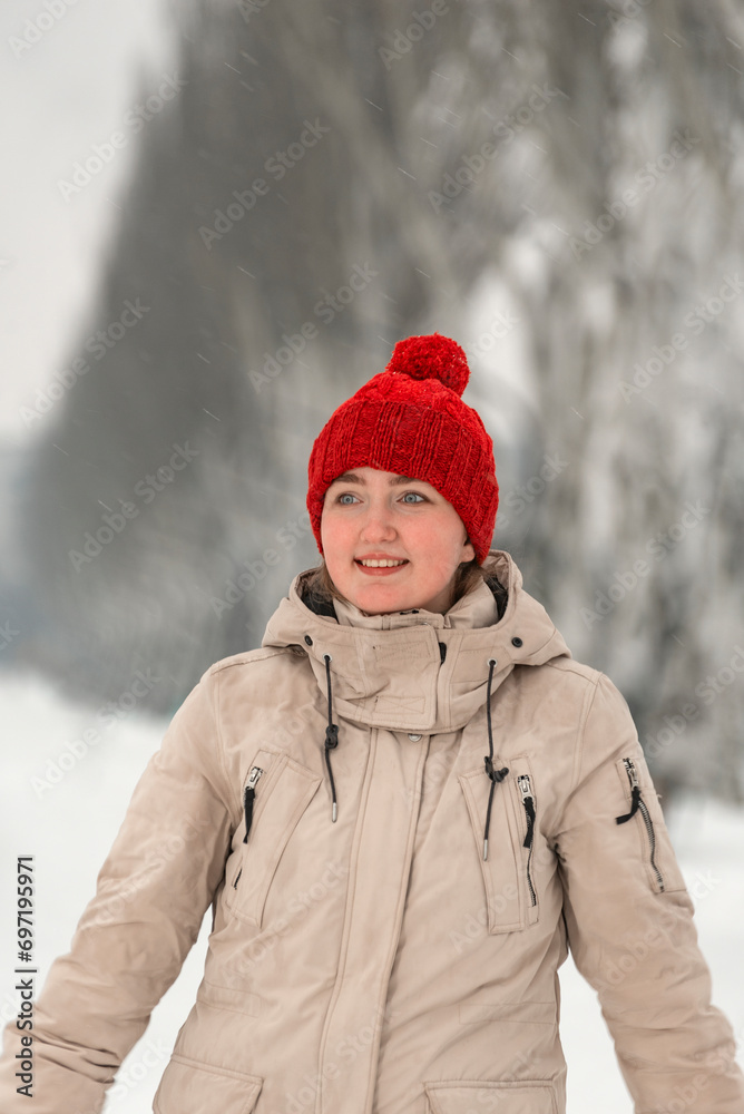 Obraz premium Portrait of beautiful girl in fashionable down jacket and knitted red hat with bubo thoughtfully looking into distance outside in winter
